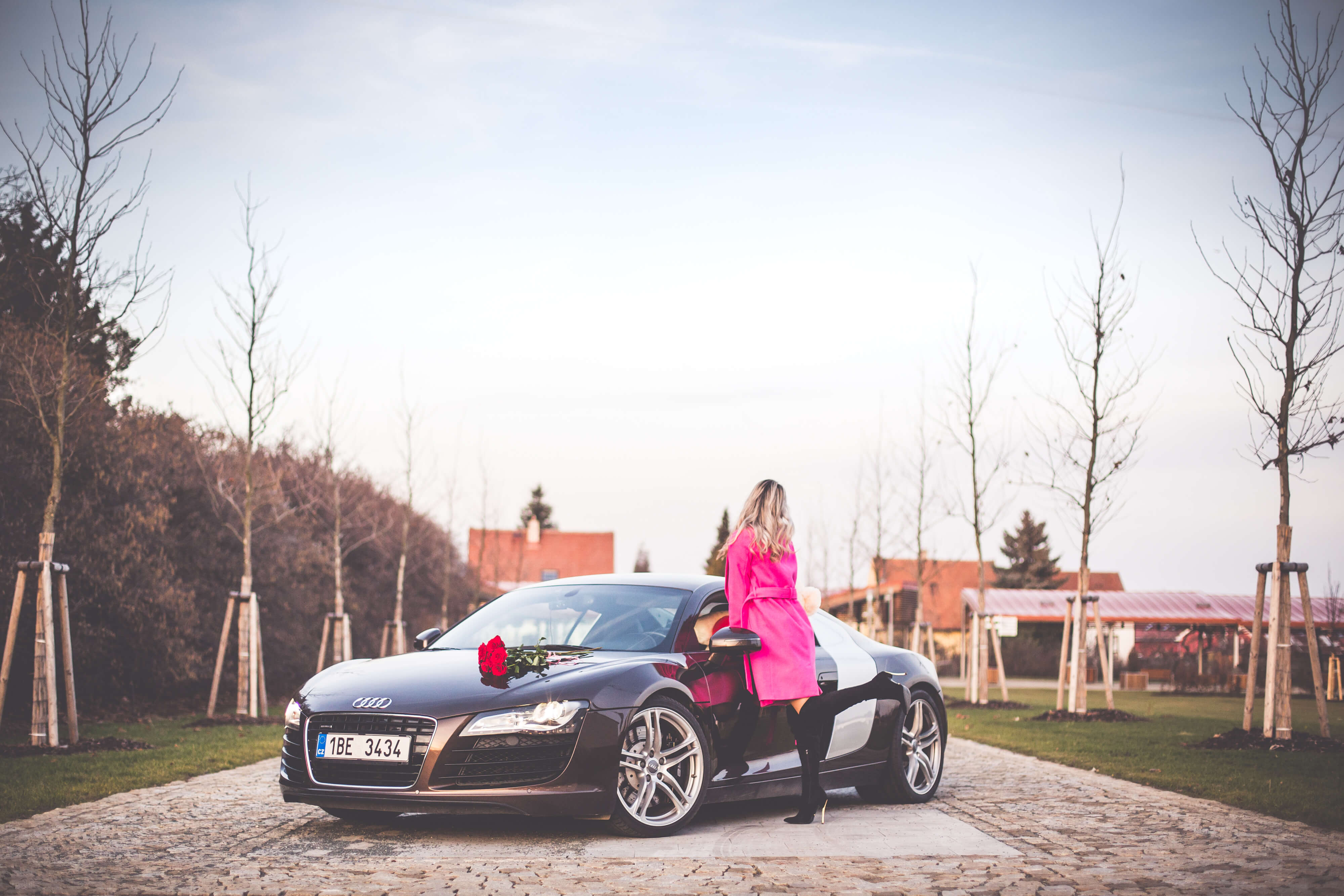 woman in pink coat standing next to sports car
